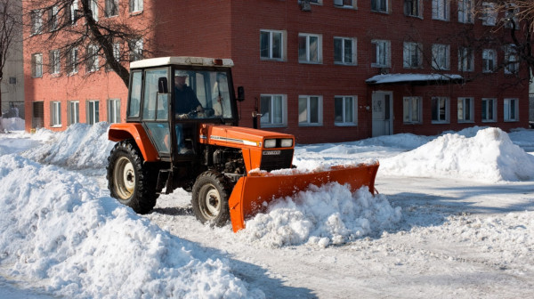 Ciągnik z pługiem usuwa śnieg z parkingu